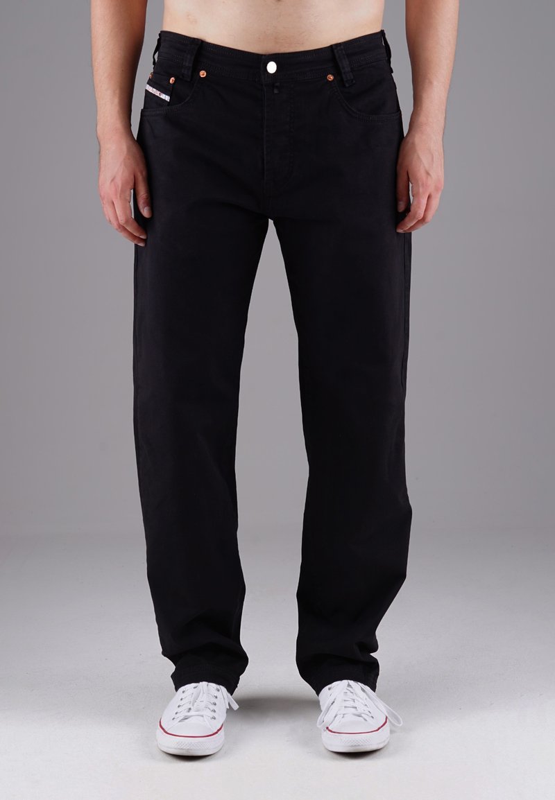 Schwarze Denim-Jeans mit geradem Schnitt, ausgestattet mit Kupferriegeln, Vordertaschen und einem Knopfverschluss. Getragen mit weißen Turnschuhen.