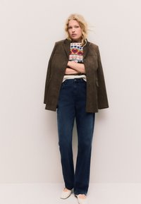 Rudos spalvos zomšinė striukė, raštuotas megztinis, tamsiai mėlynos džinsinės kelnės ir balti batai. Tiesios kelnės ir lygių tekstūrų sluoksniuotas aprangos derinys.