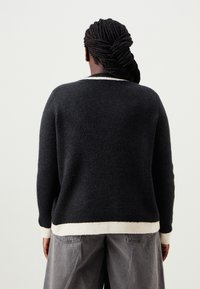 Μαύρο μάλλινο πουλόβερ με κρεμ ραβδωτό περιθώριο και μανσέτες. Ο σχεδιασμός διαθέτει χαλαρή εφαρμογή και στρογγυλή λαιμόκοψη, όπως φαίνεται από πίσω.