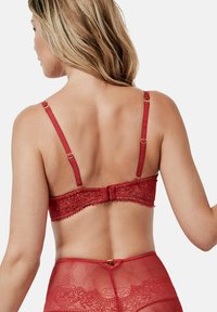 Rode kanten BH met geborduurde details, verstelbare bandjes en een haak-en-oogsluiting aan de achterkant. Zachte textuur en decoratieve afwerking aanwezig.
