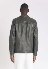Olijfgroene leren jas met een getailleerde snit, voorzien van een klassieke kraag, lange mouwen en nette stiksels langs de naden.