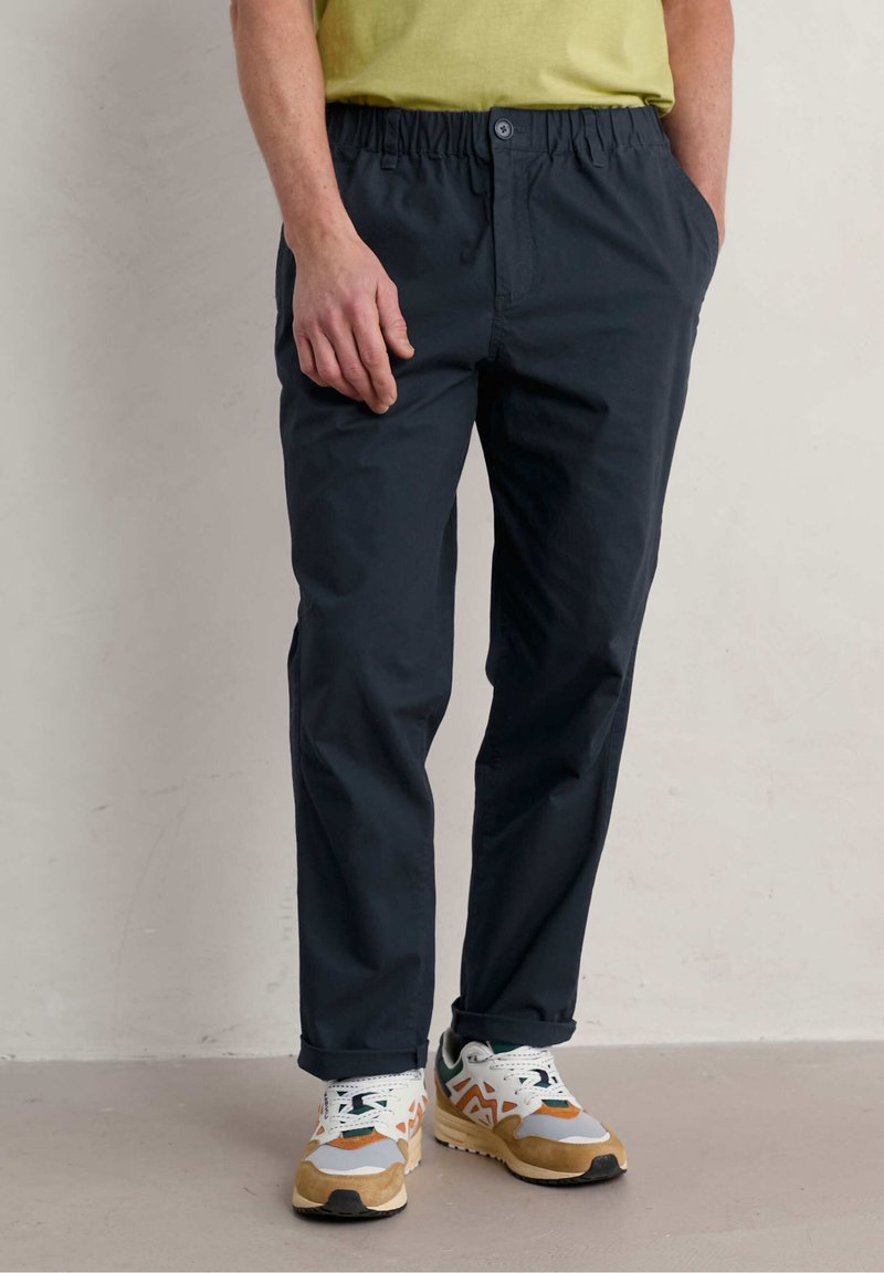 Pantalones azul marino con cintura elástica, bolsillos laterales y un corte relajado. Combinados con zapatillas multicolores y una camiseta verde claro.