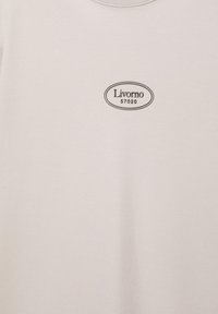 Tissu blanc avec un petit logo ovale noir indiquant "Livorno 57020" centré sur la surface.