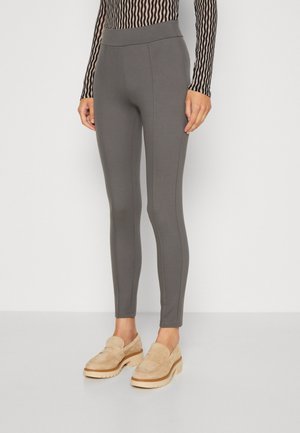 Graue Leggings aus dehnbarem Material, mit einem hohen Bund, figurnahem Design und vertikalen Nahtdetails. Getragen mit beigen Loafers.