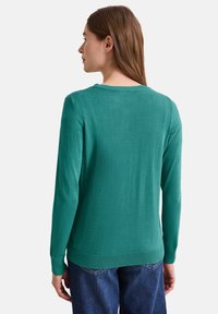 Türkiser Pullover mit langen Ärmeln, gerippten Bündchen und rundem Halsausschnitt, aus einem weichen Strickmaterial gefertigt. Getragen mit blauen Jeans.