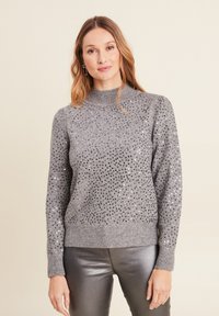Grauer gestrickter Pullover mit verzierten Pailletten, hohem Kragen, gerippten Bündchen und Saum, kombiniert mit schimmernden silbernen Hosen.