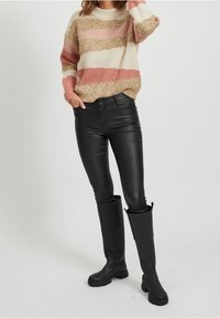 Neulepaita, jossa on leveitä vaakaraitoja väriltään kerma, vaaleanpunainen ja kulta, yhdistettynä mustiin nahkahousuihin ja polvenkorkuisiin mustiin saappaisiin.