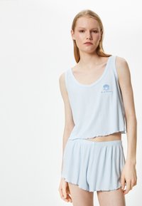 Lys blå ribbet pajamasæt bestående af en �ærmeløs cropped top og flagrende shorts, med en bølget kant og broderet muslingelogo.