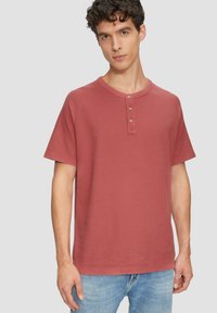 Roestkleurig T-shirt met korte mouwen, ronde halslijn en drie-knoopsluiting, gemaakt van textuurachtig katoen.