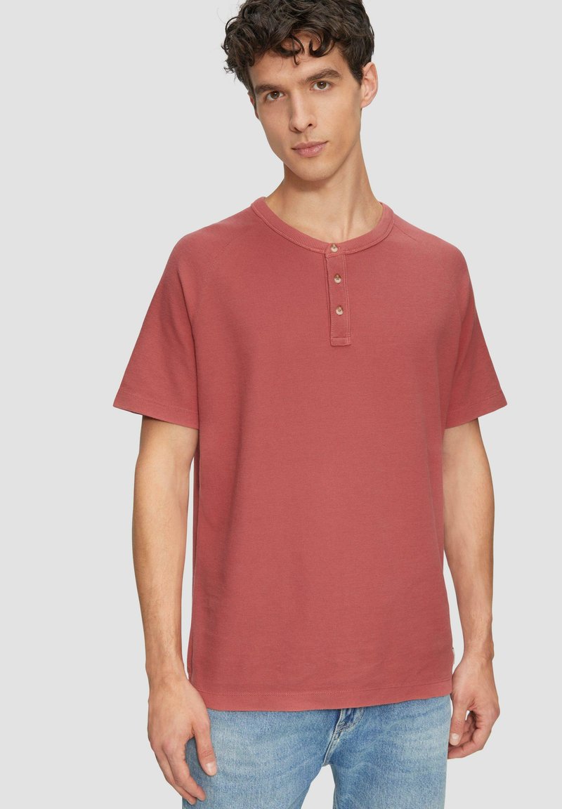Roestkleurig T-shirt met korte mouwen, ronde halslijn en drie-knoopsluiting, gemaakt van textuurachtig katoen.