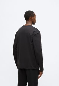 Czarna koszula z długim rękawem wykonana z miękkiej bawełny, z okrągłym dekoltem, luźnym krojem i minimalistycznym designem bez widocznych wzorów czy logo.