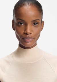 Beżowy, dopasowany golf z prążkowanym kołnierzem i gładką fakturą; posiada bezszwowe ramiona i miękki, lekki materiał.