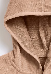 Beige huva i tyg med mjukt, texturerat material och ett ribbat mönster. Inkluderar en slät kant längs huvan öppning.