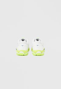 Λευκά αθλητικά παπούτσια με πράσινες λεπτομέρειες, υφασμάτινη υφή και επενδεδυμένη σόλα, με λογότυπο κοντά στη φτέρνα και δομημένο σχεδιασμό.