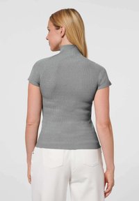 Grijs geribbeld topje met een hoge kraag en korte mouwen, aansluitend ontwerp dat de textuur accentueert. Gepaard met witte broek.