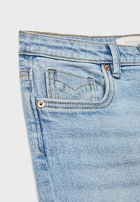 Ljusblå denimbyxor med en traditionell femficksdesign, koppardetaljer och subtila slitageeffekter på tyget.