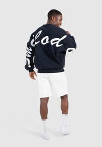 Sudadera de gran tamaño en color navy con texto en cursiva blanca en las mangas, combinada con pantalones cortos blancos. Presenta puños y dobladillo acanalados, además de un corte relajado.