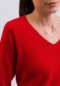 Maglione rosso con scollo a V, realizzato in materiale morbido, caratterizzato da una trama liscia e maniche lunghe.