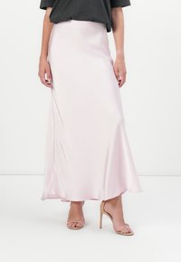 Saia maxi de cetim rosa, design fluido em A. Textura suave, comprimento até ao joelho com drapeado subtil. Combinada com sandálias de salto alto nude.