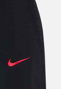 Tissu noir avec un logo Nike en forme de swoosh rouge brodé près d'une couture et d'une ouverture de poche.