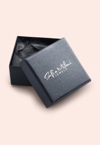 Boîte à bijoux rectangulaire noire avec un extérieur texturé, partiellement ouverte pour révéler du papier de soie noir à l'intérieur ; présente un logo blanc sur le dessus.