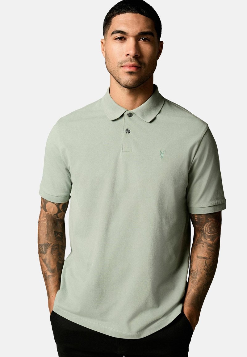 Polo de color verde menta con cuello y dos botones. Presenta un pequeño emblema bordado en el lado izquierdo del pecho. Tejido suave y ligero.