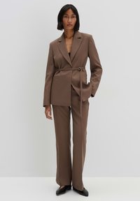 Completo marrone su misura composto da un blazer con cintura e pantaloni a campana, realizzato in tessuto liscio, con lapel classico e tasche laterali.