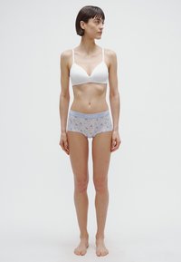 Beli brezžični modrček in spodnje hlačke s cvetličnim vzorcem in svetlo modrim pasom. Gladek tekstura, oprijeta zasnova. Model brez čevljev.