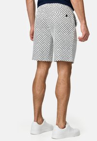 Pantalones cortos blancos con un patrón geométrico negro, hechos de una tela ligera, con bolsillos laterales y una cinturilla ajustable.