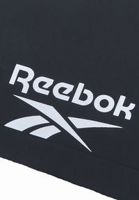 Zwarte stof met het Reebok-logo in opvallend wit. Het ontwerp bevat gestileerde accenten die het logo kruisen en beweging suggereren.