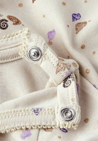 Beżowy materiał z małymi, kolorowymi wzorami muszelek w odcieniach fioletu, brązu i złota. Zawiera srebrne zatrzaski i teksturowane wykończenie.