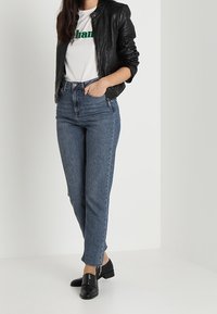 Černá kožená bunda, bílý tričko se zeleným textem, modré džíny s vysokým pasem a černé mokasíny se zipy. Úhledný, ležérn í outfit.