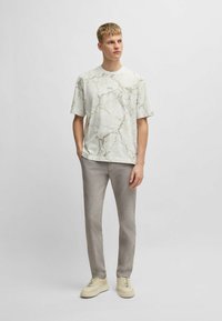 Kortärmad skjorta i vitt med marmor mönster, kombinerad med ljusgrå strukturerade byxor och krämfärgade sneakers.