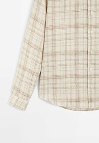 Camicia beige con maniche lunghe, caratterizzata da un leggero motivo a tartan nei toni del marrone e crema. Realizzata in tessuto testurizzato, con orlo arrotondato e botttoni.