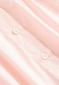 Tissu rose doux avec deux boutons blancs cousus alignés verticalement sur un matériau lisse, légèrement froissé.