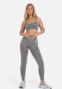 Lichtgrijze sportbeha en bijpassende hooggerokte leggings, met een textuurontwerp en een logoaccent op de tailleband.