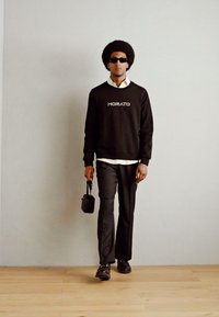 Sudadera negra con el logo "MORATO", camisa blanca con cuello debajo, pantalones negros, gafas de sol y un pequeño bolso negro, combinado con zapatos elegantes.