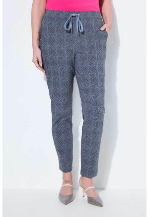 Kvinde iført tætsiddende gråspraglede bukser med snøre i taljen og lyserød top, kombineret med spidse hæle med ankelremme.