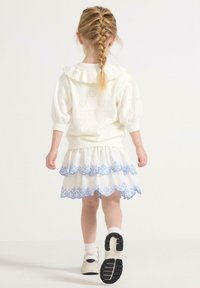 Hvid kjole med pufærmer, flæsede krave, hjerteudskæringer og blå broderet kant. Båret med hvide sneakers og hvide sokker.