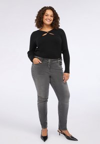Maglietta nera a maniche lunghe con dettagli tagliati, abbinata a jeans skinny grigi con borchie laterali e scarpe con tacco a punta nere.