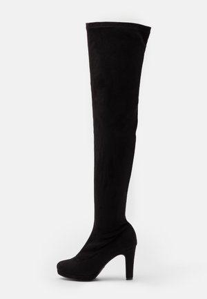 Svarta högsteppade stilettokängor i mjukt mockamaterial med rund tå och hög, kraftig klack. Slät yta utan synliga dekorationer.