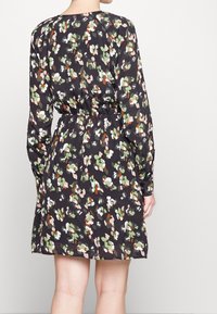Czarna sukienka w kwiatowy wzór w kolorach zielonym, białym, pomarańczowym i różowym. Posiada długie rękawy oraz taliowanie dla dopasowanego kroju. Miękka tekstura tkaniny.
