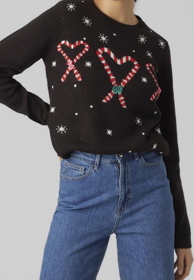 Pull noir en tricot orné de motifs en forme de cœurs de cannes en bonbon et de flocons de neige, assorti à un jean en denim. Le pull a un col rond et des poignets côtelés.