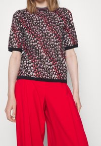 Kurzärmliges Strickoberteil in Schwarz mit einem strukturierten Muster aus rosa und weißen Blumen, einem gerippten Rundhalsausschnitt und schwarzem Saum.