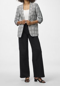 Grå och svart rutig blazer med avslappnad passform, krage och uppvikta ärmar, i kombination med högmidjade svarta vida byxor.