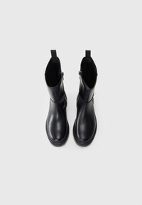 Sorte skinn ankle boots med glatt tekstur, rund tå, stablet hæl og glidelås på siden, med trekkleser for enkel påkledning.