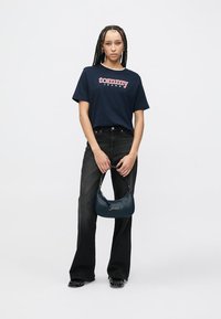 Camiseta de algodón azul marino con el logo "tommy", vaqueros negros de corte recto y bolso de cuero azul marino con asa de cadena plateada.