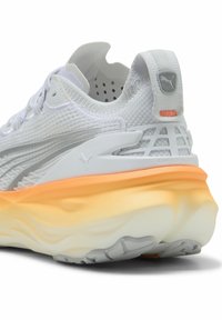 Scarpa da ginnastica bianca con tomaia testurizzata, accenti grigi e intersuola di colore arancione. Presenta una suola robusta con motivo di aderenza.
