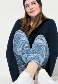 Marinblå långärmad tröja, mönstrade blå joggingbyxor med djurmotiv och ränder, som har en bekväm passform. Vita sneakers fulländar looken.