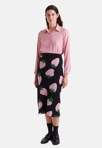 Camisa de manga larga rosa combinada con una falda midi negra con un estampado de fresas en rosa y verde, llevada con accesorios negros.